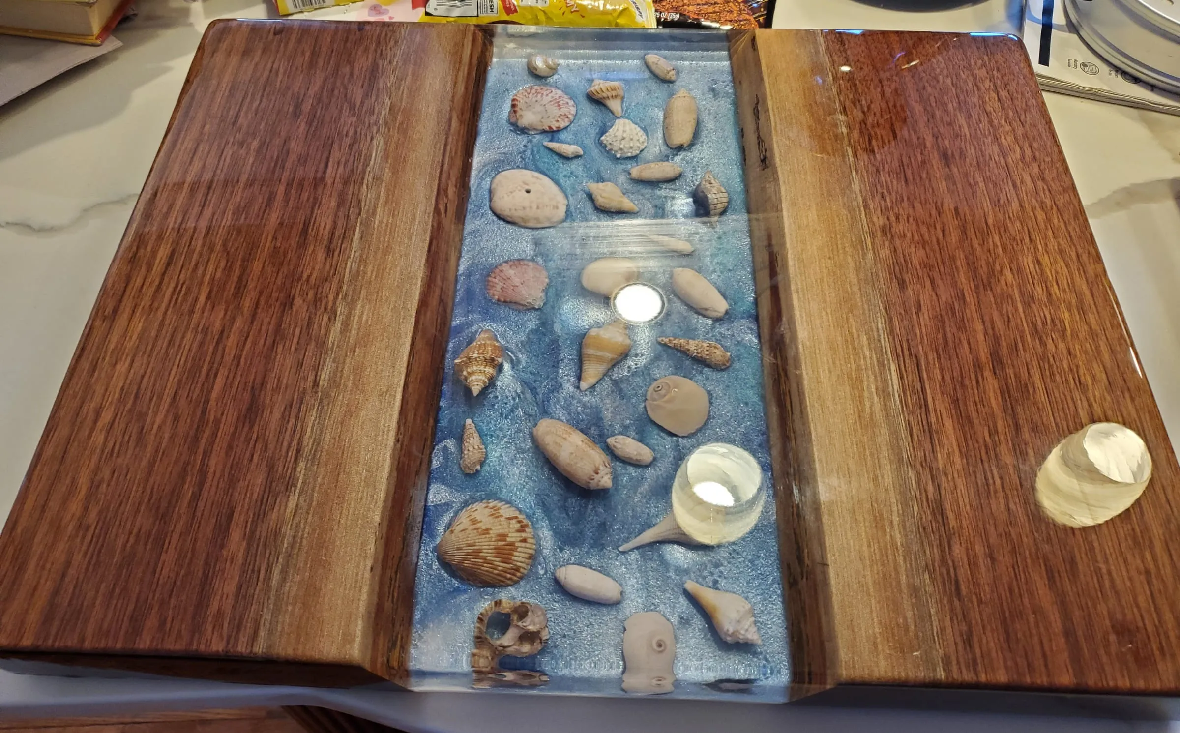 River Shell Trays — Shells and stones in a river between glossy dark slabs